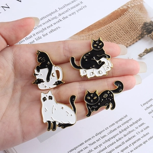 Set of four black and white cat enamel pins with moon and star accents on a hand