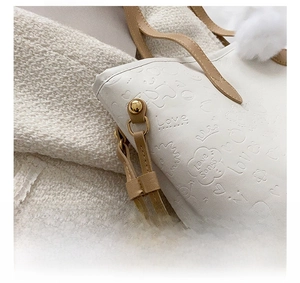 Detail of gold metal hardware and embossed cartoon leather pattern on white tote bag