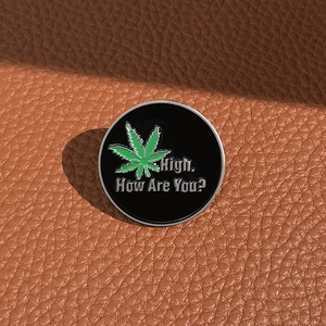 Macro detail of round enamel pin with green leaf design and High How Are You text