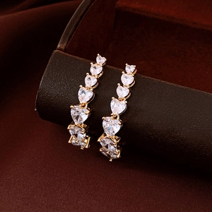 Detailed macro view of gold plated heart shaped zircon tassel earrings on dark background