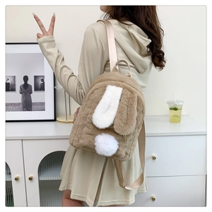 Girl wearing a khaki and white plush bunny backpack with 3D ears in a cozy room