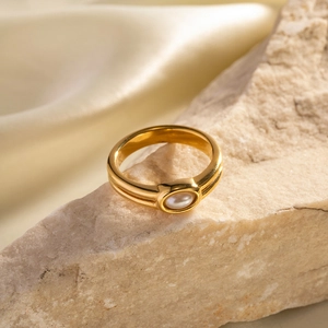 Close-up of a double-layered 18k gold ring with an oval pearl on a stone surface