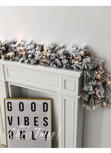 Close-up of snow-flocked Christmas garland with pine cones and LED lights on a mantel
