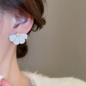 Boucle d'oreille fleur en émail blanc portée avec détails dorés et texture scintillante