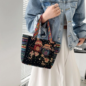 Detailed embroidery of two owls on a floral branch upon a black canvas tote bag