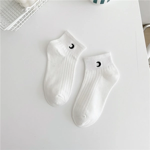 Detail of white cotton ankle sock with black crescent moon pattern on white desk
