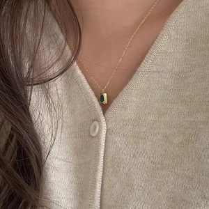 Close-up of gold choker necklace with emerald green rectangular pendant on neck