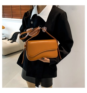 Detail of a brown shoulder bag with a unique wave-curve flap shown in an elegant interior