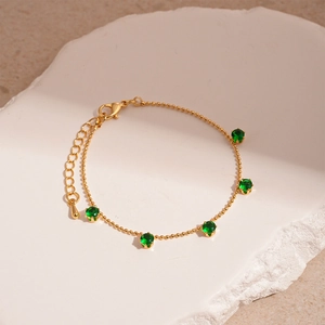 Detail of gold beaded bracelet with five green cubic zirconia stones on white stone tray