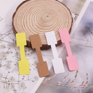 Detail shot of dumbbell-shaped paper jewelry tags in four colors on a wooden background
