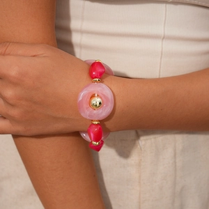 Detail of pink and magenta resin beads on a gold necklace worn over a beige sweater