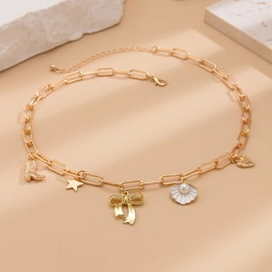 Golden chain necklace featuring bow, shell, heart, boot, and star charms on stone props