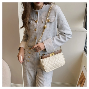 Detail of cream quilted bag with brown leather trim and golden chain strap for women