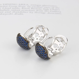 Macro shot of silver huggie earrings with deep blue pavé zircon and hollow geometric patterns