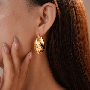 Detail of gold-tone geometric textured earrings featuring a hollowed-out lattice pattern