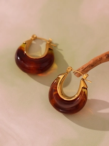Detailed view of amber resin hoop earrings with golden metal clasps on a branch