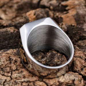 Two-tone stainless steel men's skull ring with gold geometric accents on wood background