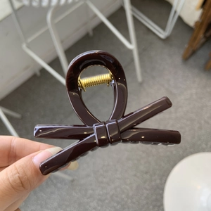 Detail of dark brown resin bow hair clip with gold metal spring and glossy finish