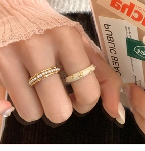 Detail of stacked gold pearl ring and cream enamel band with star studs for women