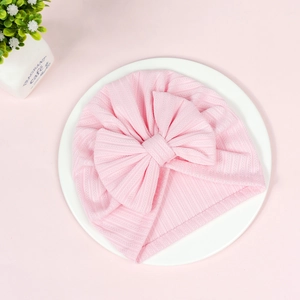 Close-up of pink ribbed baby turban hat with a large decorative bow on a white plate