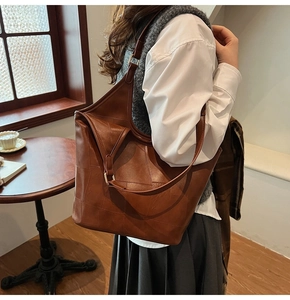 Grote bruine leren tote bag met stiksels aan de schouder gedragen door een model in huis