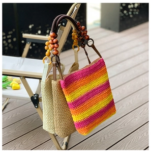 Close-up of rainbow striped straw bucket bag with wooden bead handle on a wooden deck
