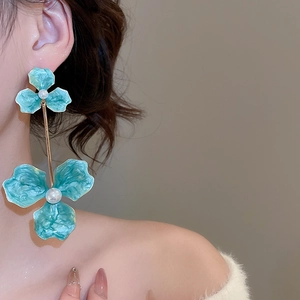 Detail of long floral drop earrings with lake green petals and white pearls on a model