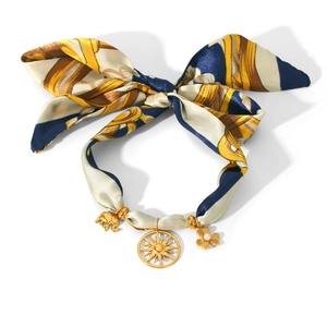 Close-up of a blue and yellow silk ribbon necklace with gold sun, clover, and elephant charms