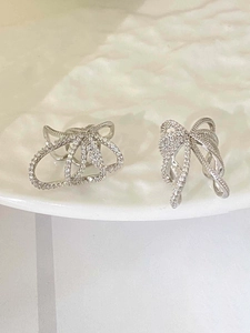 Detail view of silver bow-shaped stud earrings with zircons on a white plate