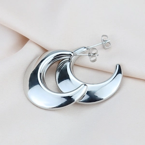 Macro shot of silver crescent teardrop earrings with mirror-polished finish on silk