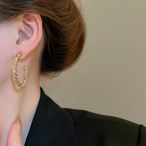 Close-up of gold twisted rope C-shaped hoop earrings worn by a female model