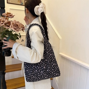Detail of a black floral quilted tote bag with a cream lace scrunchie in a cozy indoor setting