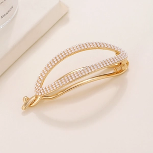Close-up of elegant gold metal hair clip with inlaid white pearls on beige background