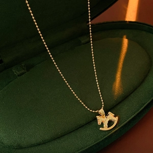 Gros plan d'un collier pendentif cheval à bascule doré dans un écrin en velours vert