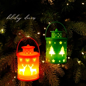 Red and green Christmas lanterns with deer and tree patterns hanging on a pine tree branch