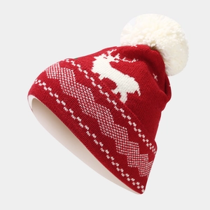 Close-up of red knit Christmas hat featuring white reindeer pattern and a fluffy pom-pom