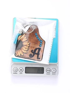 Western style sunflower and letter A leather keychain with blue tassel being weighed on scale