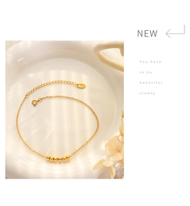 Detail view of 18K gold beaded anklet on white porcelain with elegant floral shadow