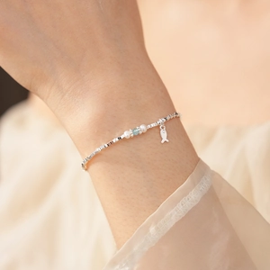 Close-up of silver beaded bracelet with pearls and a small fish charm on a model's wrist