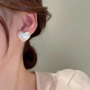 Close-up of heart-shaped pearl studs showing soft iridescent luster on the ear lobe