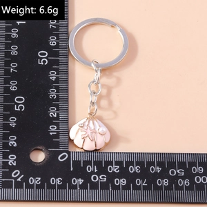 Macro detail of pink shell keychain with starfish and pearl next to measurement caliper