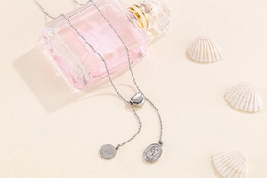 Detail of silver heart and coin pendants on a chain with elegant perfume bottle background