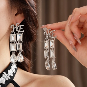 Detail of silver drop earrings with square crystals and letter charms on a model