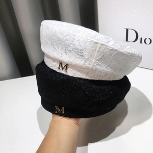 Detailed lace texture of a beret hat featuring a gold metallic M logo charm embellishment