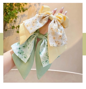 Detail of floral bow hair clip held by hand showing yellow and green fabric textures