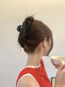Close-up of a glossy black ribbon hair claw clip holding a low bun on a model's hair