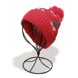 Detailed close-up of a red ribbed knit hat featuring white cherry patterns and a large pompom