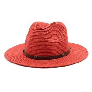 Detail view of a red straw fedora hat featuring a brown leather band with metal rivets