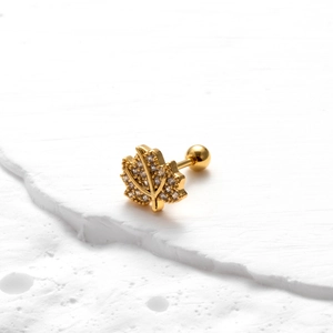 Macro shot of a gold maple leaf earring with zircon stones on a white stone background