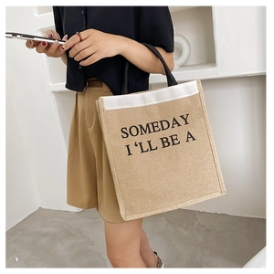 Close-up of linen tote bag with black straps and 'SOMEDAY I'LL BE A' text print